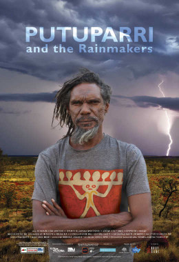An Indigenous man stands with his arms crossed in from of a desert landscape with dark skies and a lightening bolt striking ground over his shoulder.
